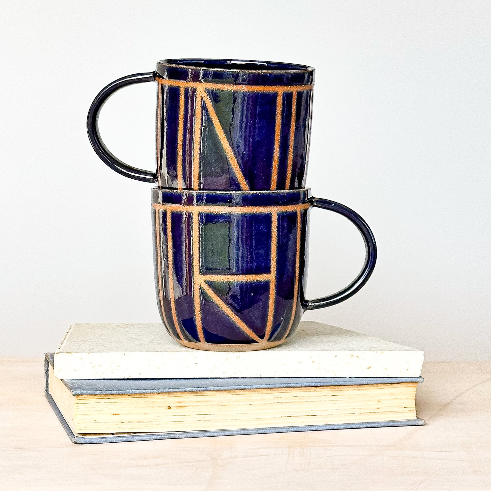 Two stacked ceramic mugs with geometric patterns on a white background