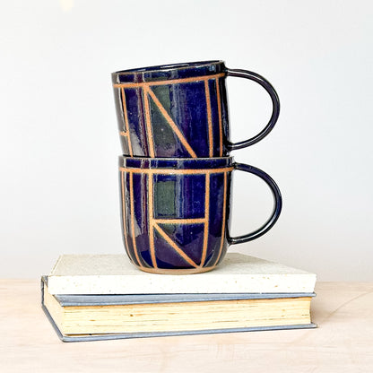 Two stacked ceramic mugs with geometric design on a white surface