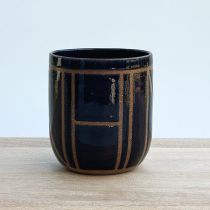 A midnight blue ceramic cup with brown geometric patterns on a light wooden surface and light background