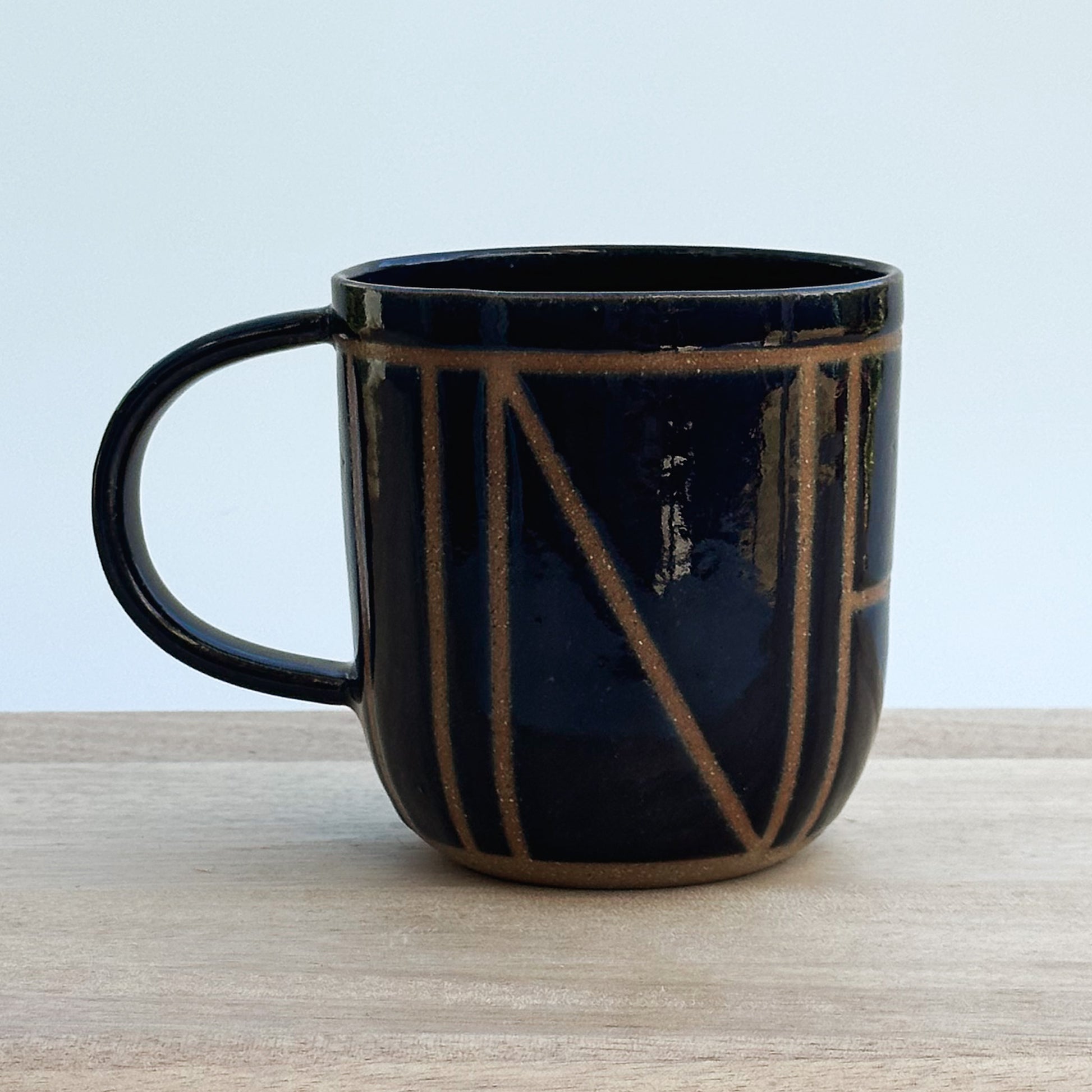 A midnight blue ceramic mug with brown geometric design on a wooden surface