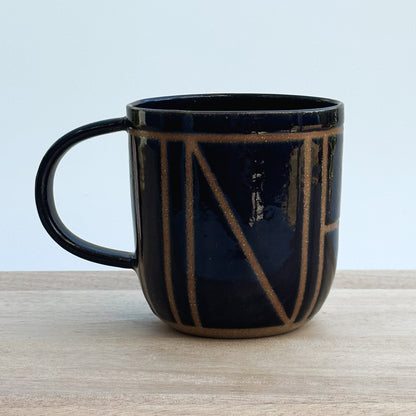 A midnight blue ceramic mug with brown geometric design on a wooden surface