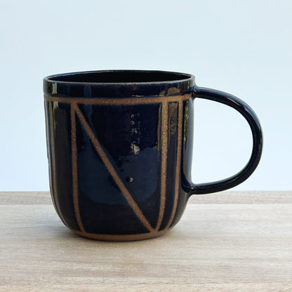 A midnight blue ceramic mug with a geometric design on a wooden surface
