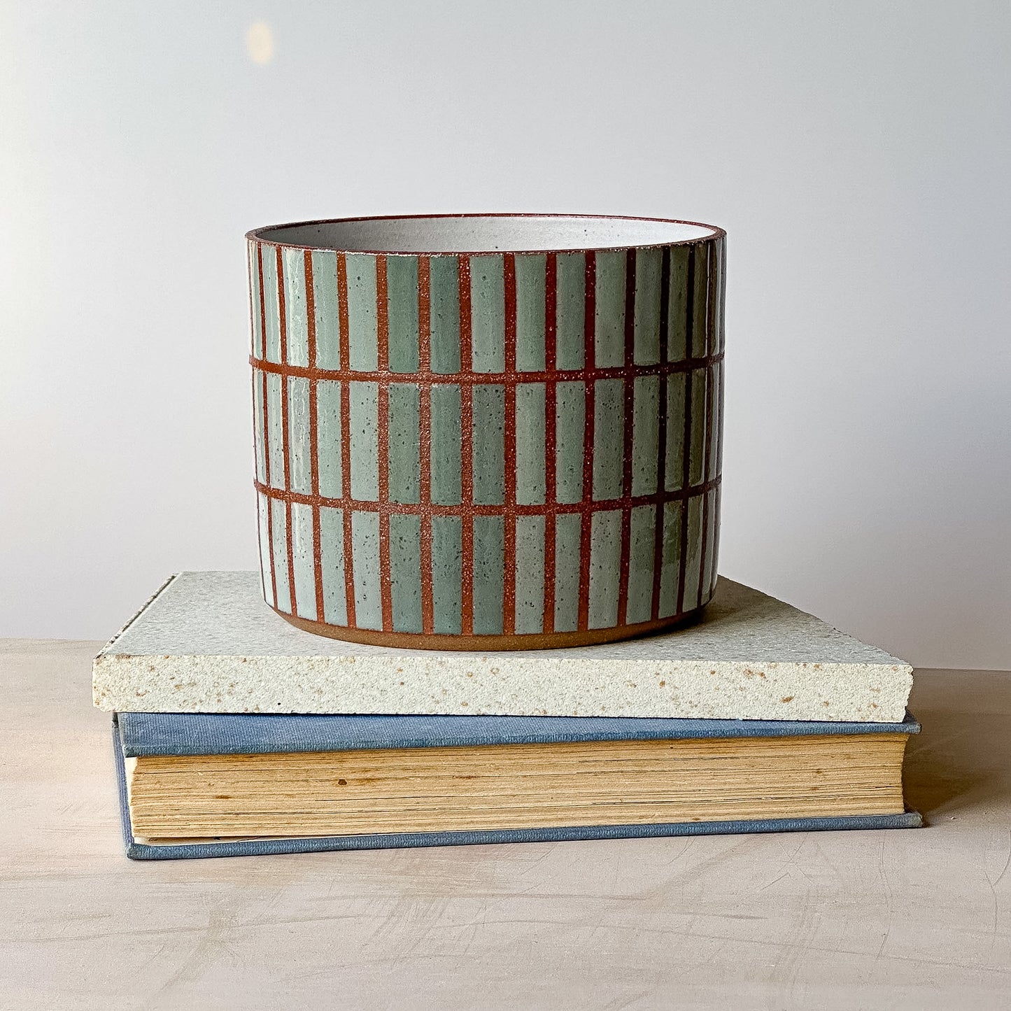 Ceramic planter with striped design on a stack of books against a plain background