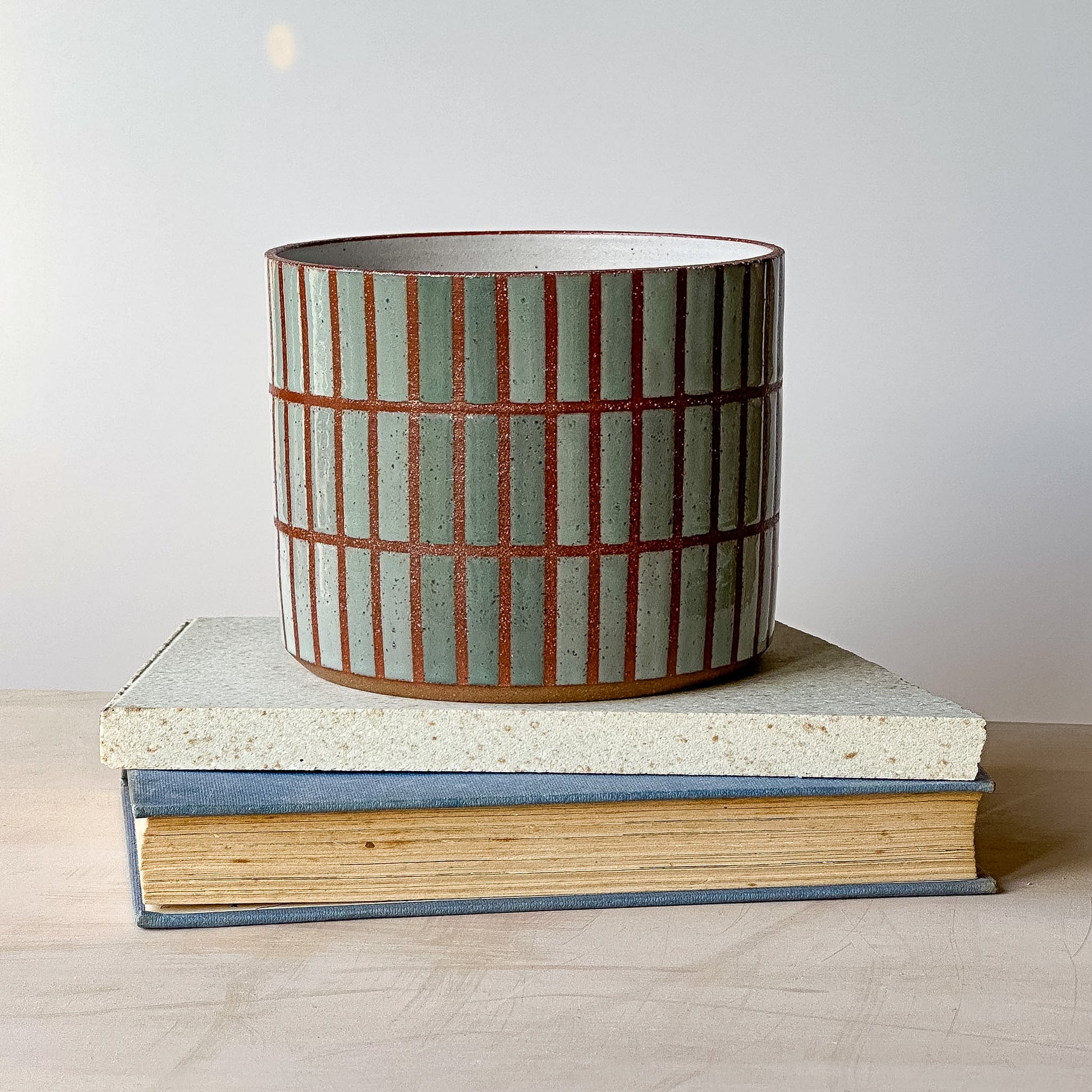 Ceramic planter with striped design on a stack of books against a plain background