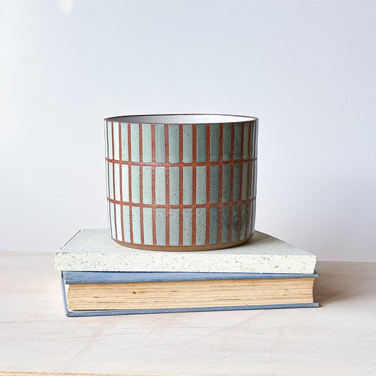 Ceramic pot with striped design on top of two books against a white background