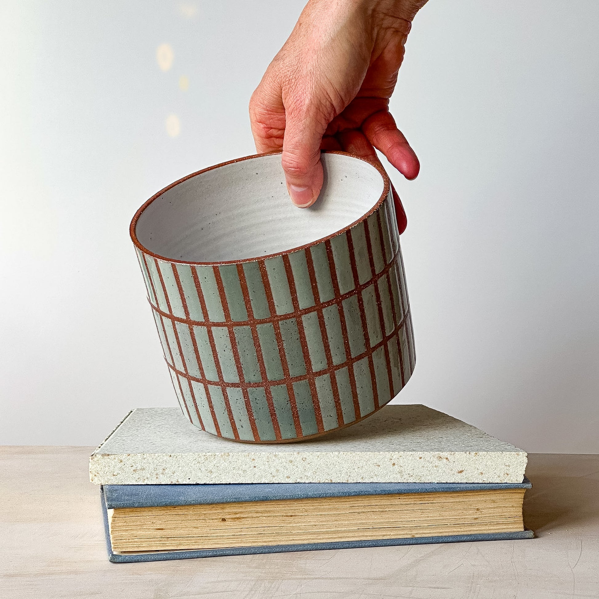Person holding a ceramic pot with striped design on top of two books