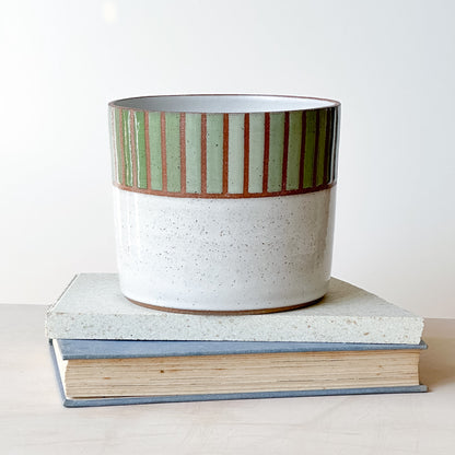Ceramic pot with striped design on top of two books against a white background