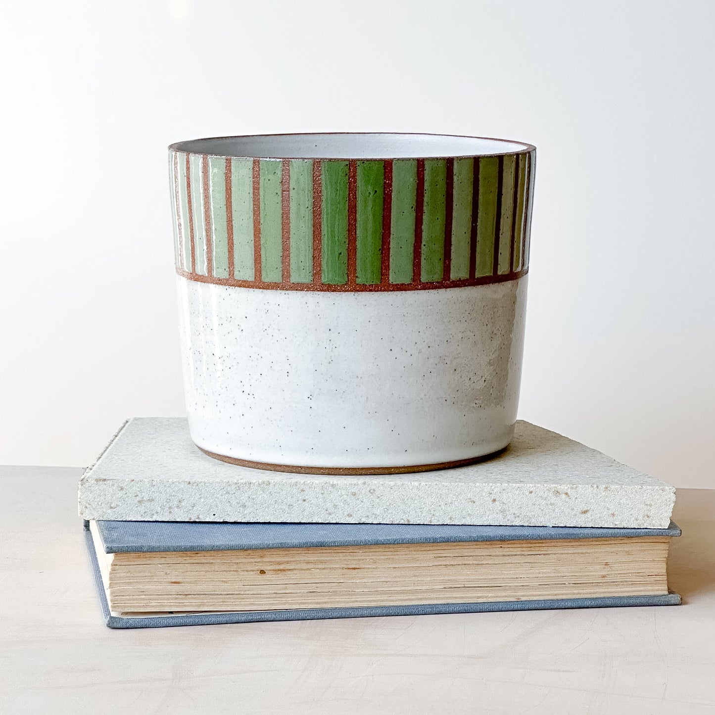 Ceramic planter with green stripes on a stack of books against a white background