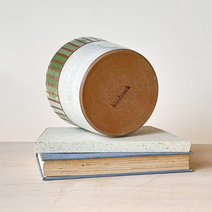 View of the base of a round ceramic planter pot with striped design on top of a book