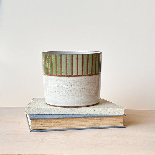 Ceramic planter with striped design on top of a book against a plain background