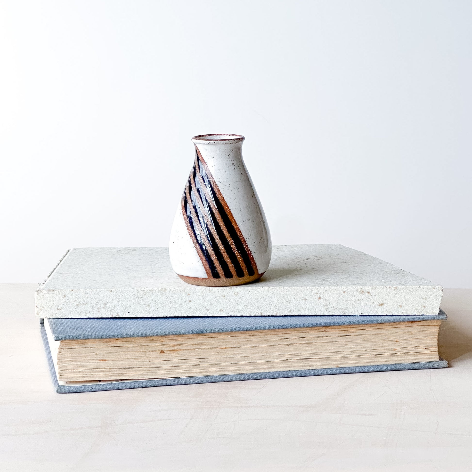 Ceramic vase with striped design on top of a book against a white background