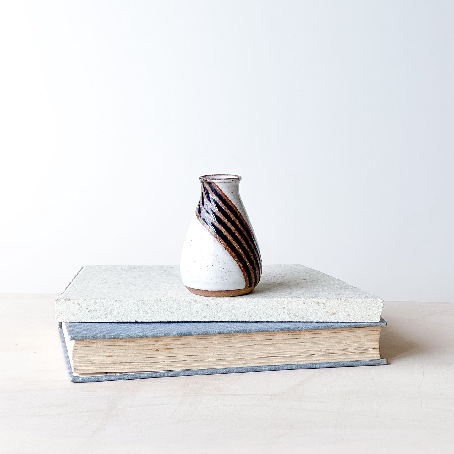 Ceramic vase with striped design on top of a book against a white background