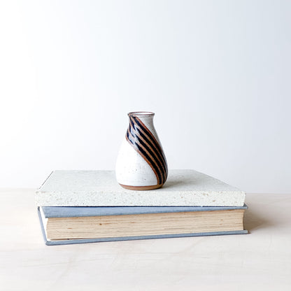 Ceramic vase with striped design on top of a book against a white background