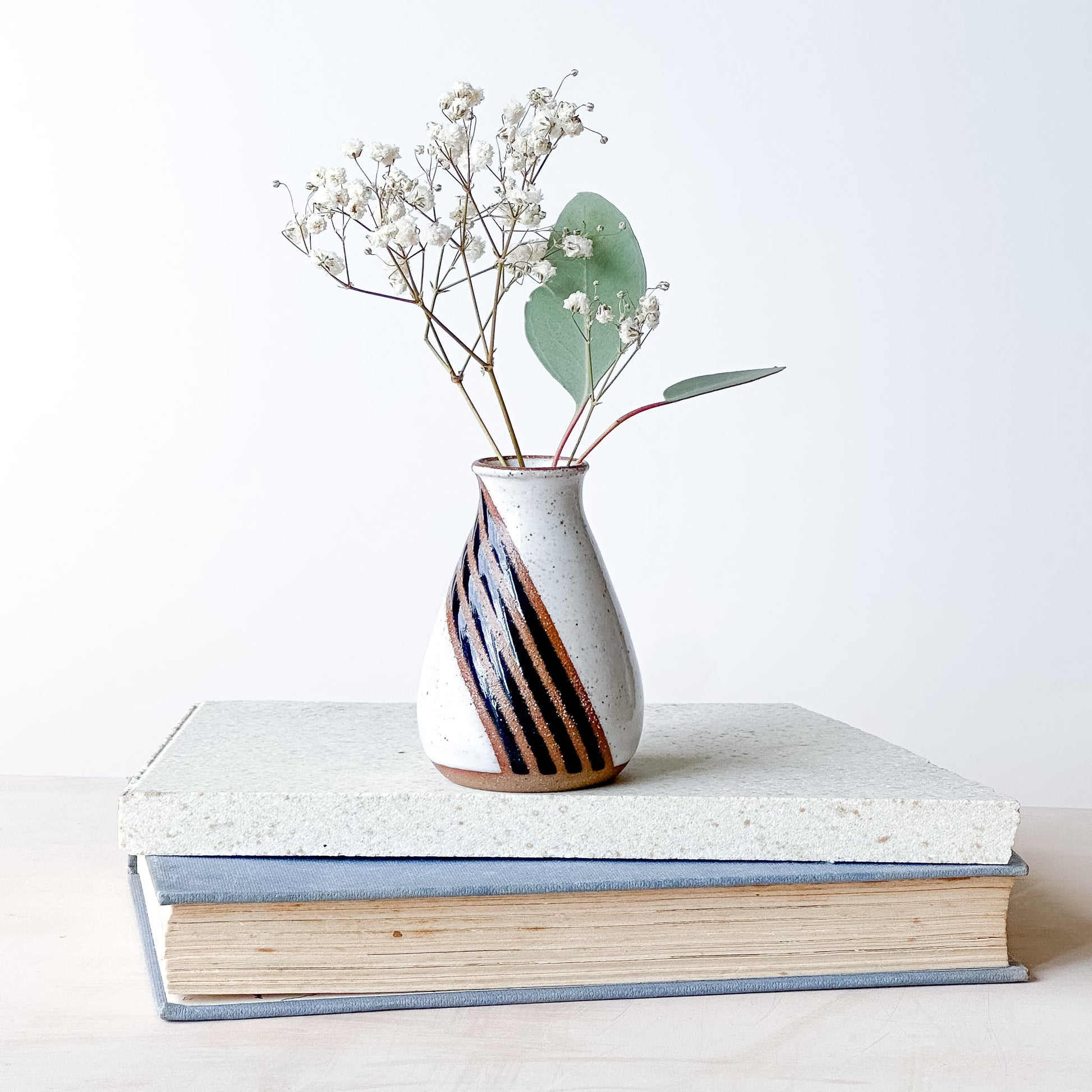 Vase with dried flowers on top of two stacked books against a white background