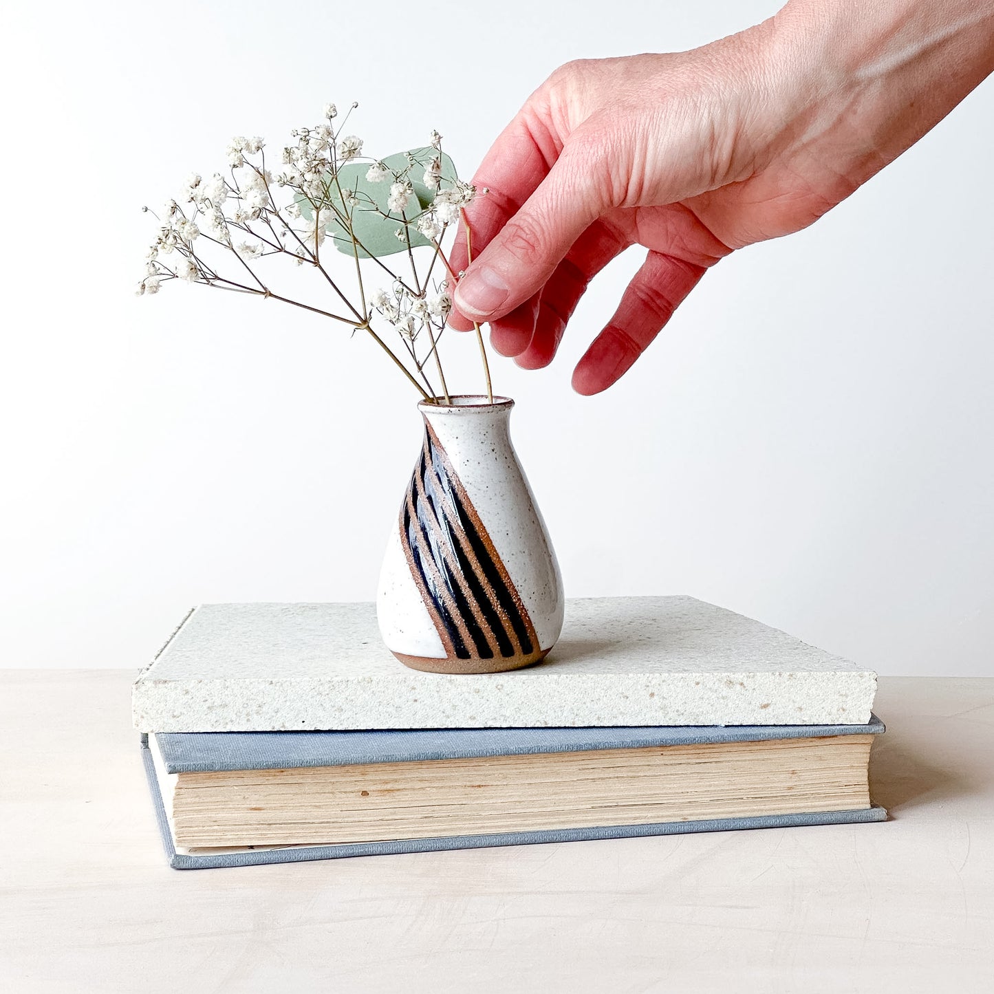 Hand placing a small vase with dried flowers on top of a book