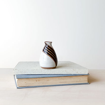 Small ceramic vase with striped design on top of a book against a plain background