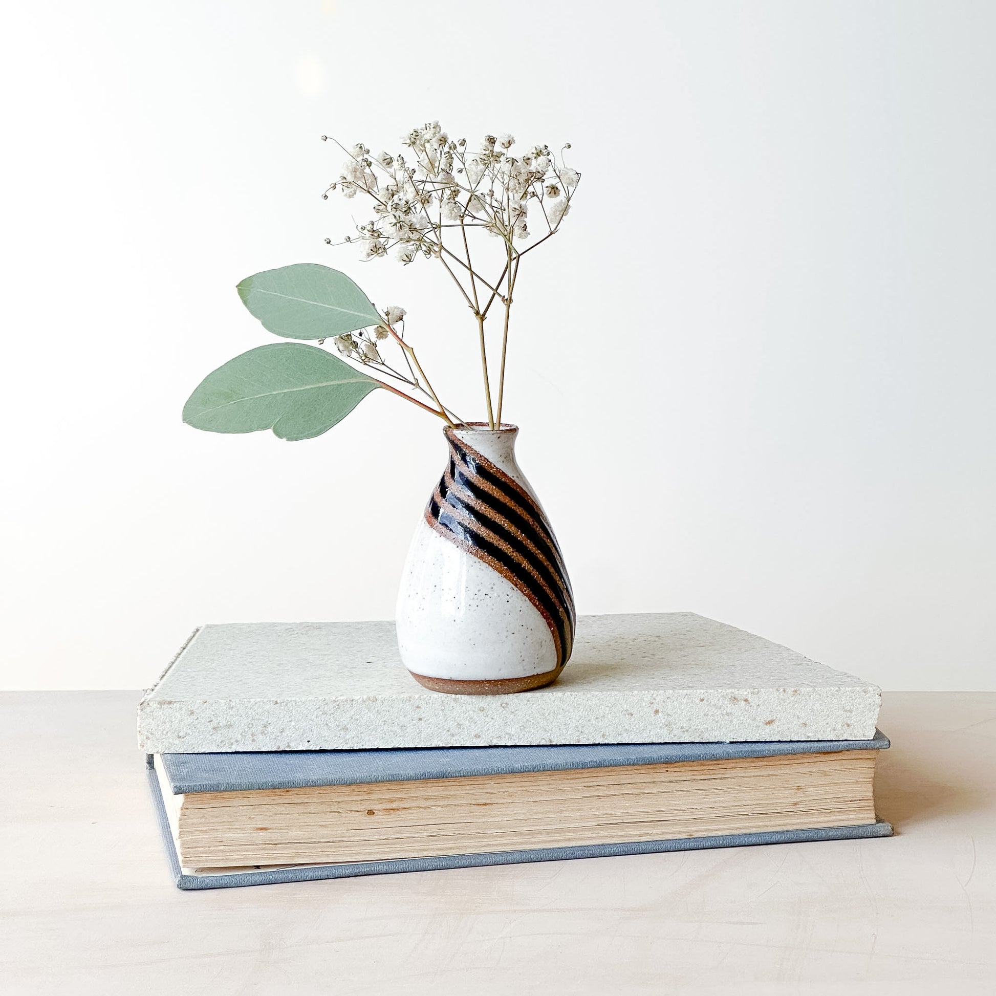Vase with dried flowers on a stack of books against a white background