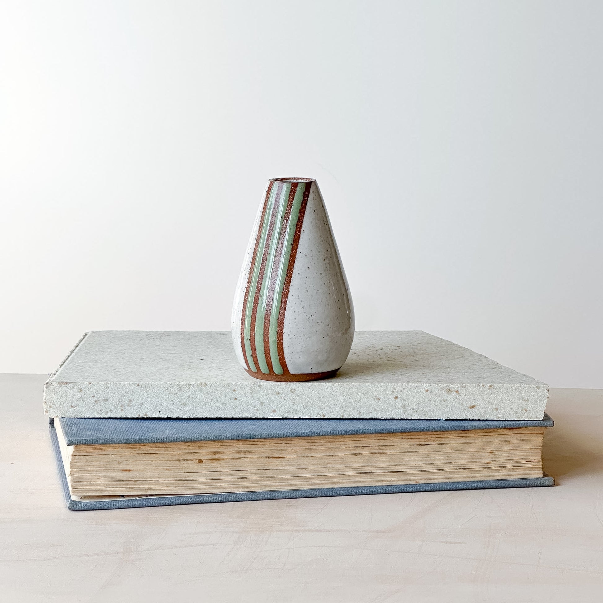 A white mini vase with green stripes on a tile and book