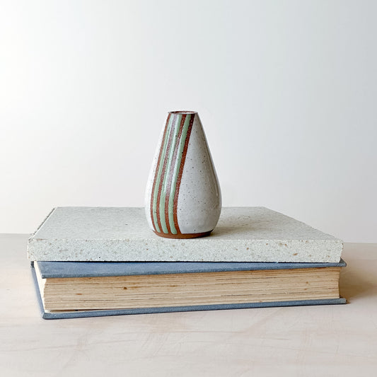 A white mini vase with green stripes on a tile and book