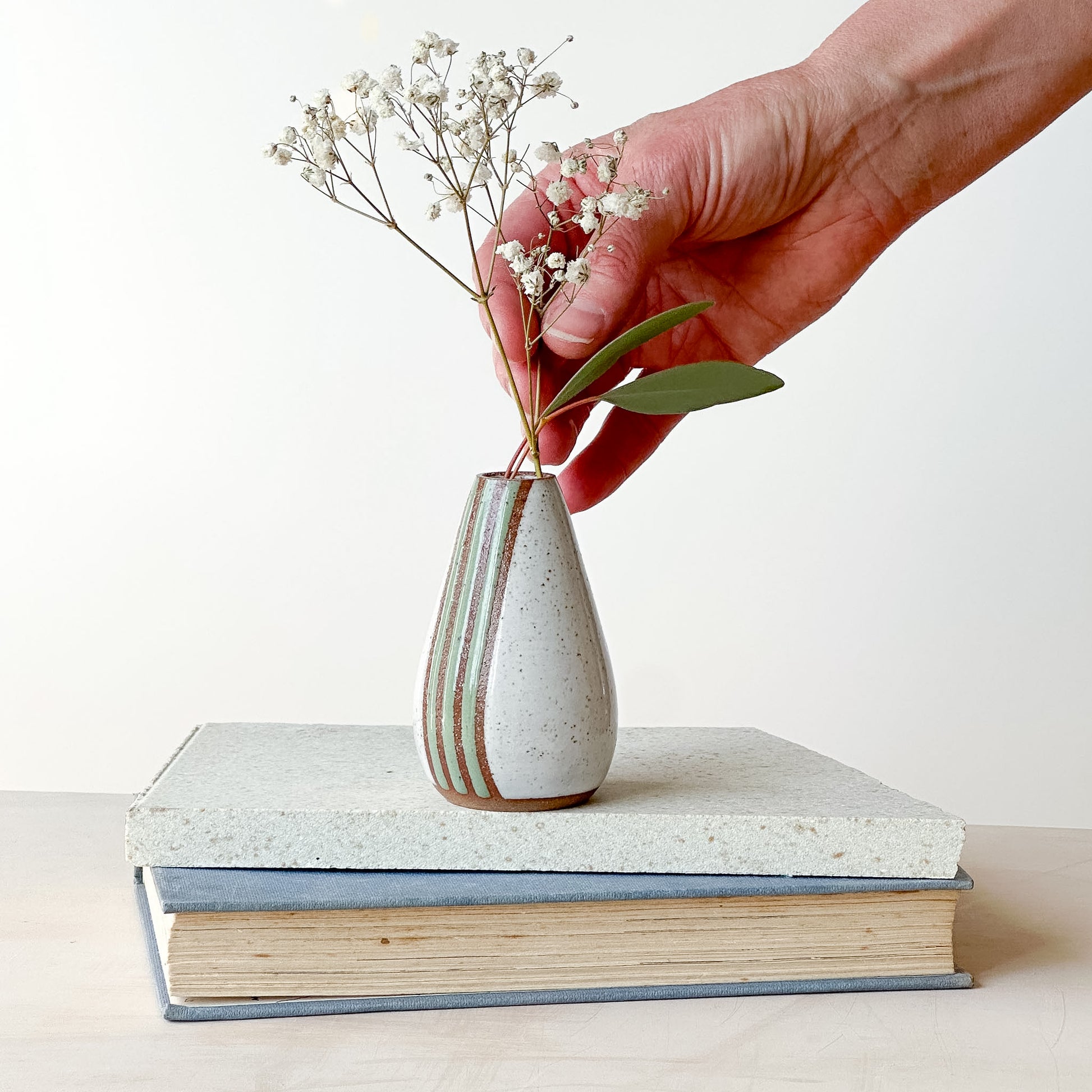 hand arranging flowers in a white and green mini vase