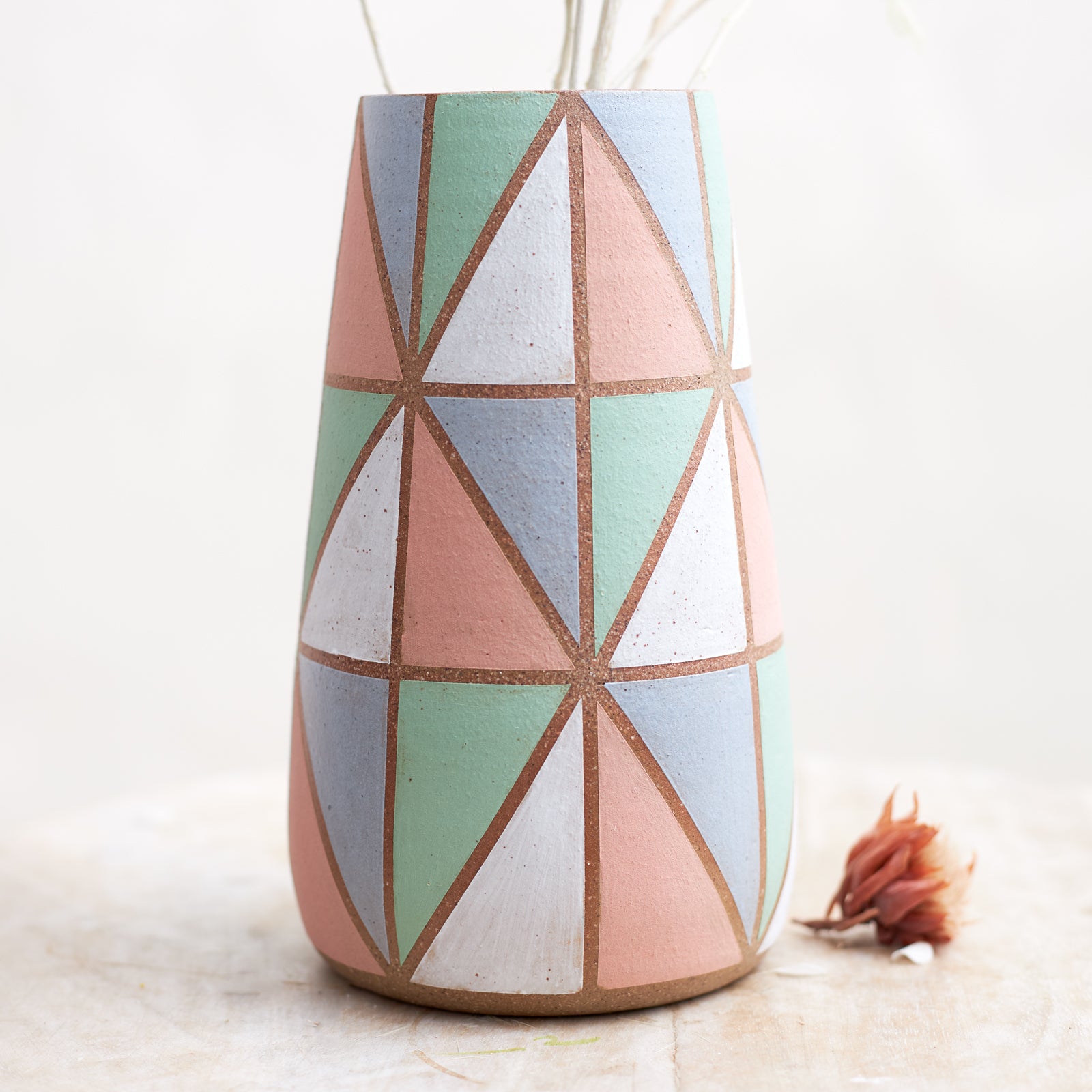 A close-up view of the Geometric Handmade Ceramic Teardrop Vase in pastel-coloured glazes. This handmade vase sits on a wooden stool.