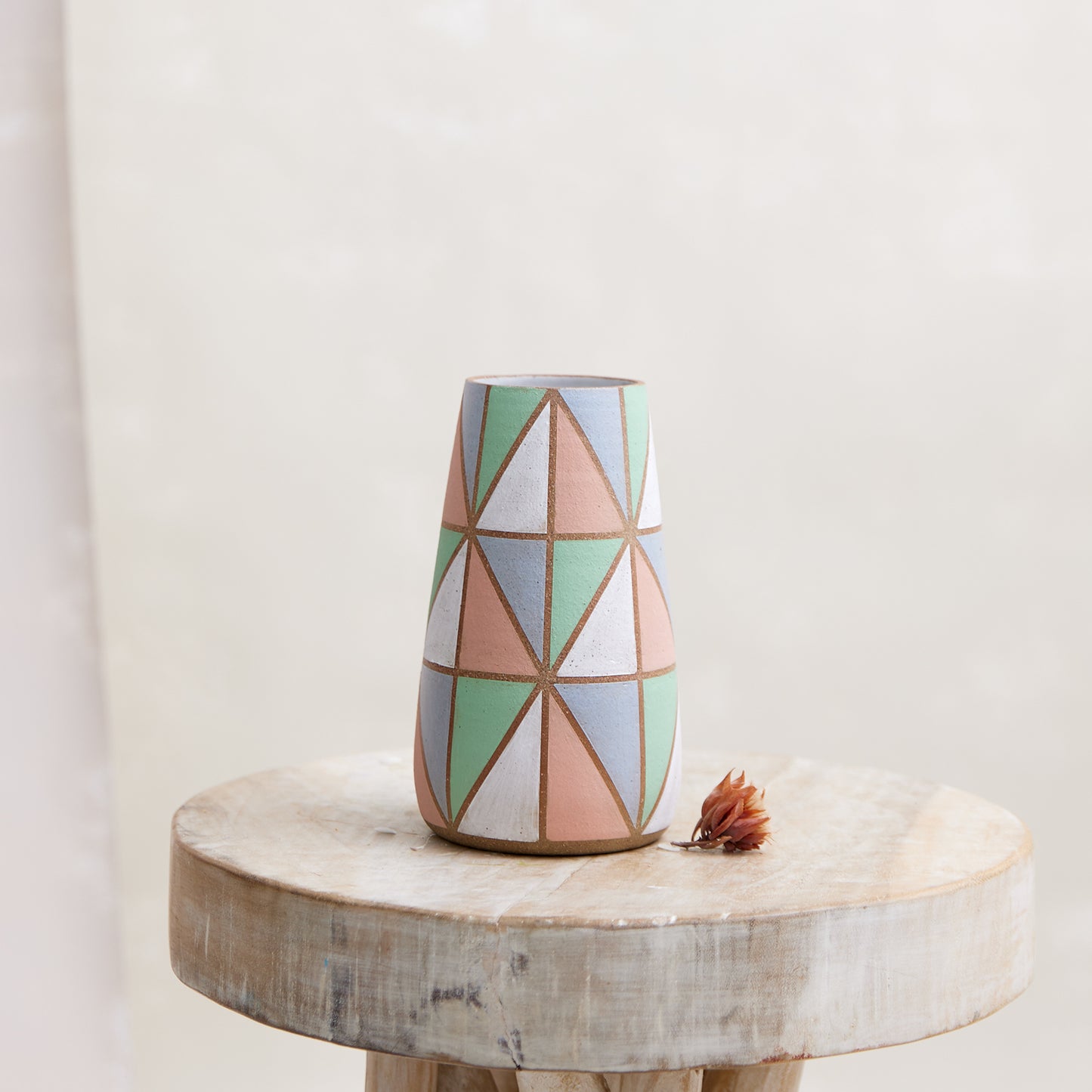 A front view of the Geometric Handmade Ceramic Teardrop Vase in pastel-coloured glazes. This handmade vase sits on a wooden stool.