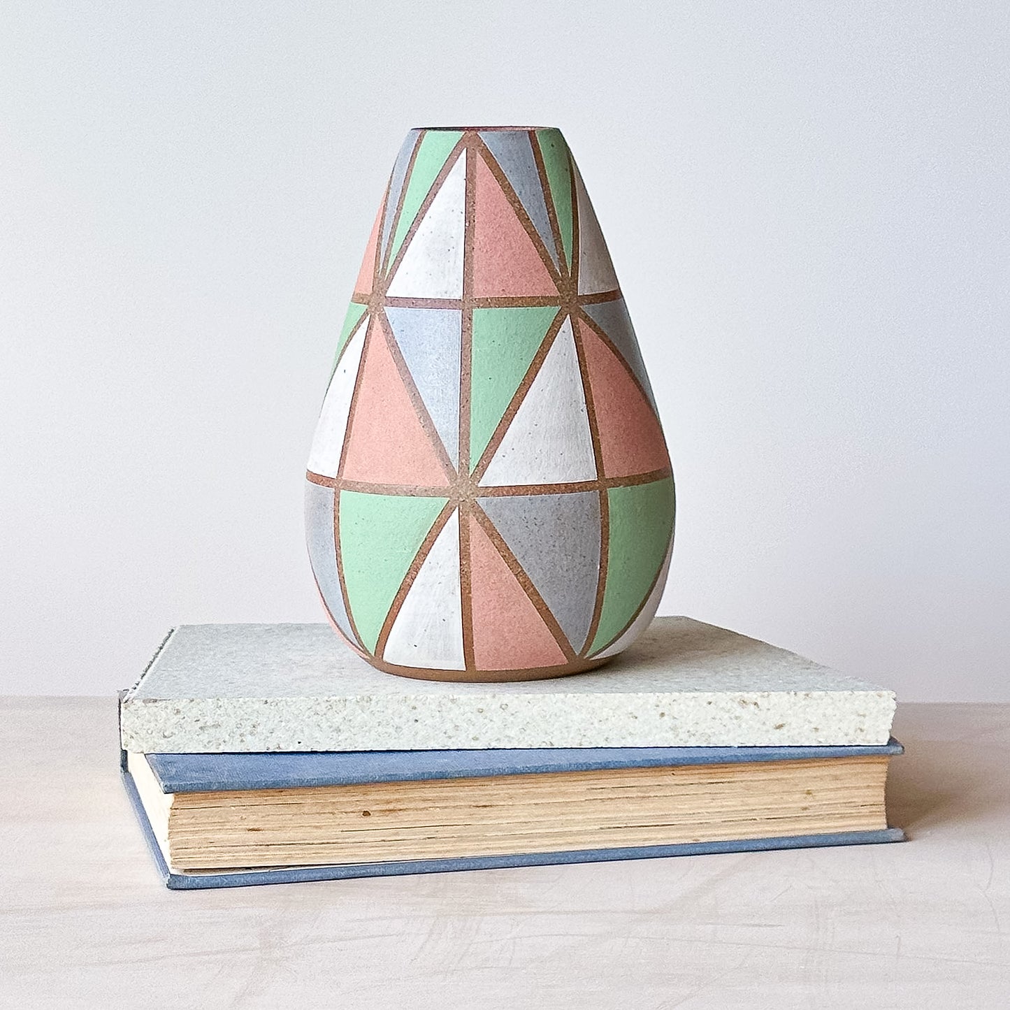 Geometric patterned vase on a stack of books with a plain background