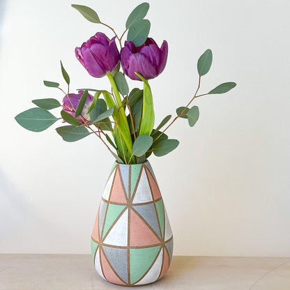 Geometric patterned vase with purple tulips and green leaves on a light background