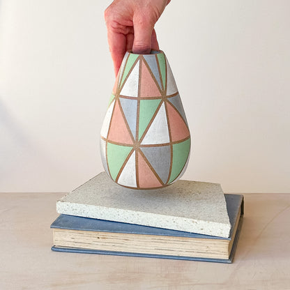 Hand holding a geometric-patterned vase on a stack of books with a plain background