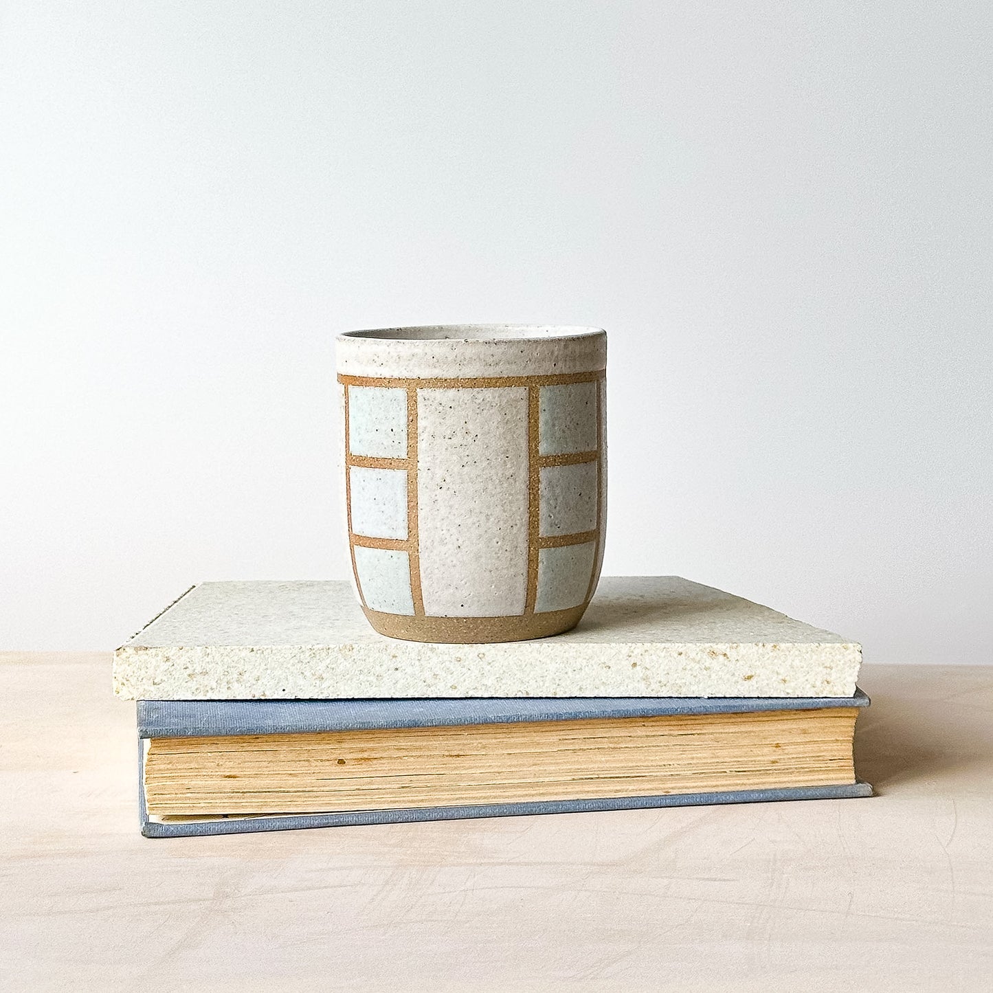 Ceramic cup with geometric pattern on top of a book against a plain background