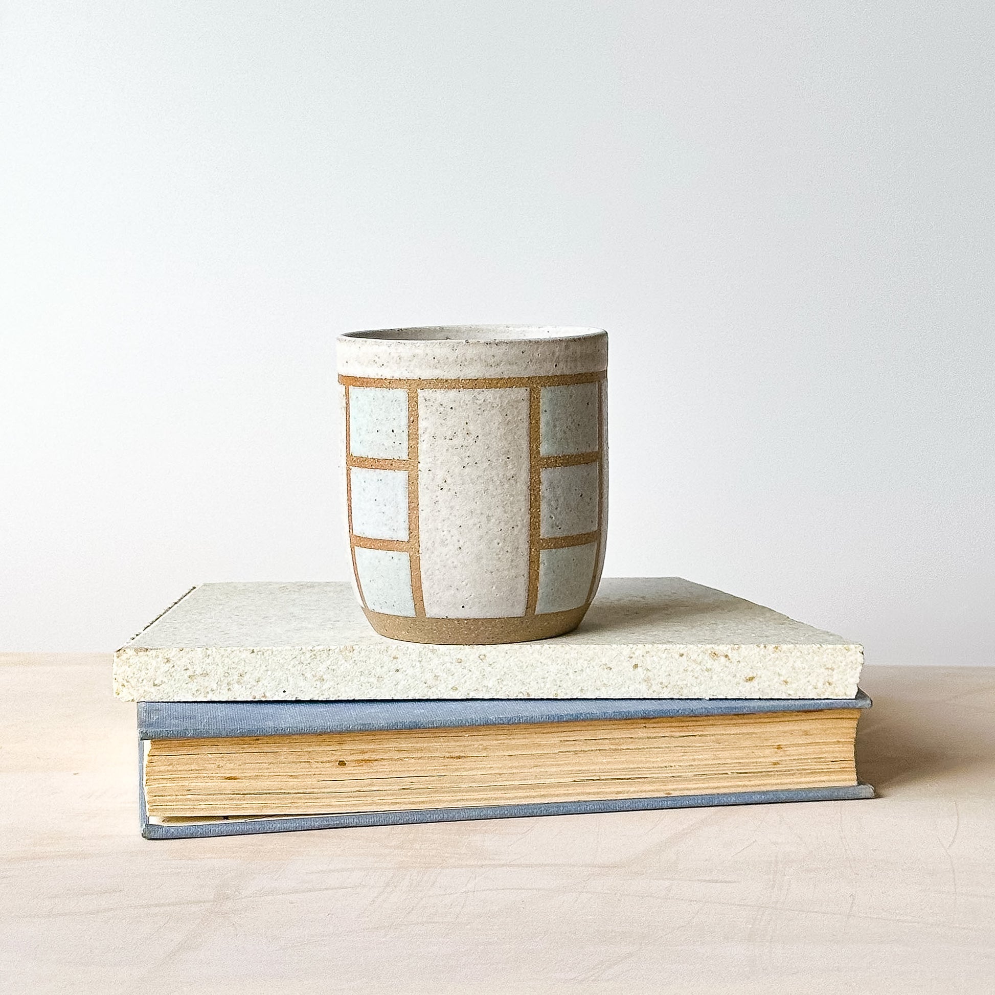 Ceramic cup with geometric pattern on top of a book against a plain background