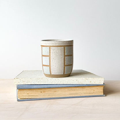 Ceramic cup with geometric pattern on top of a book against a plain background