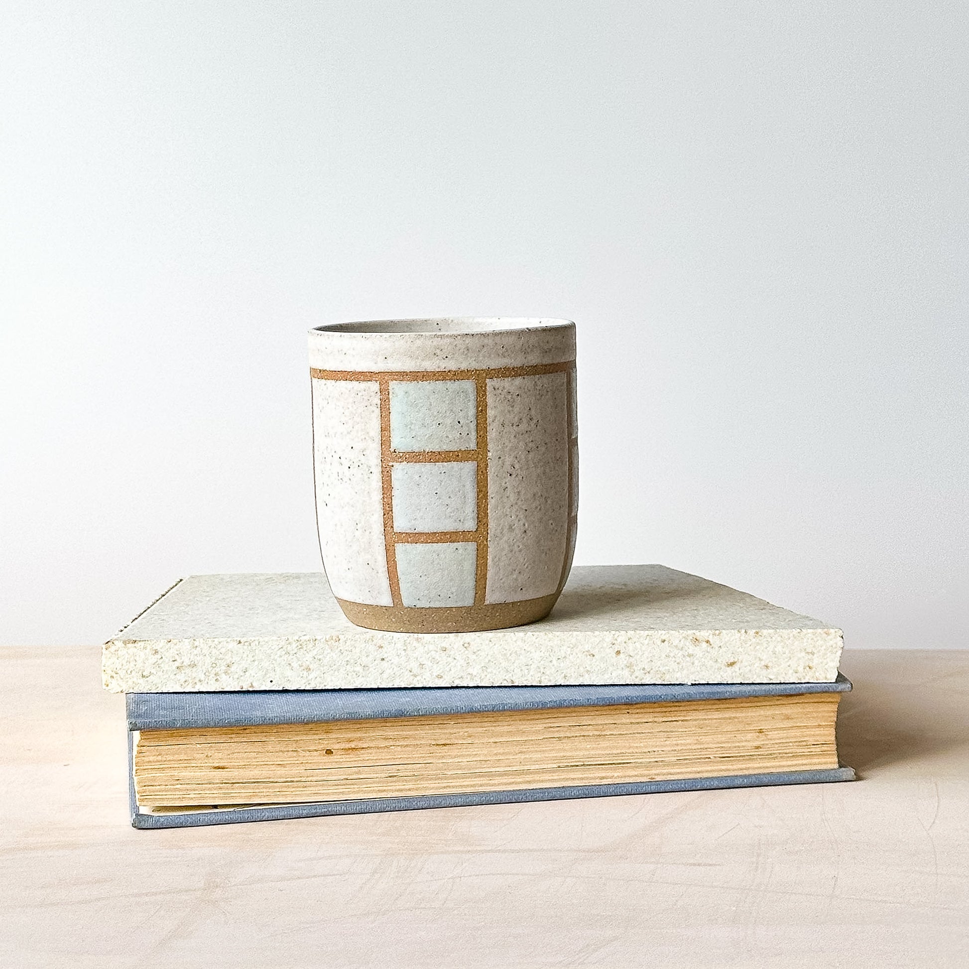 Ceramic cup with geometric pattern on a stack of books against a light background