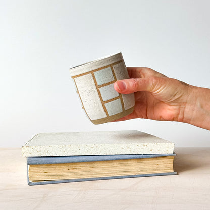 A hand holding a geometric tumbler over a tile.