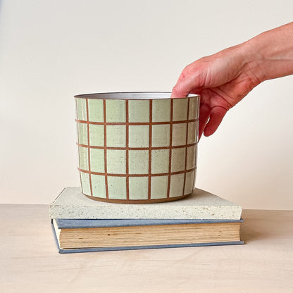 Ceramic mug with grid pattern held over a stack of books on a light background