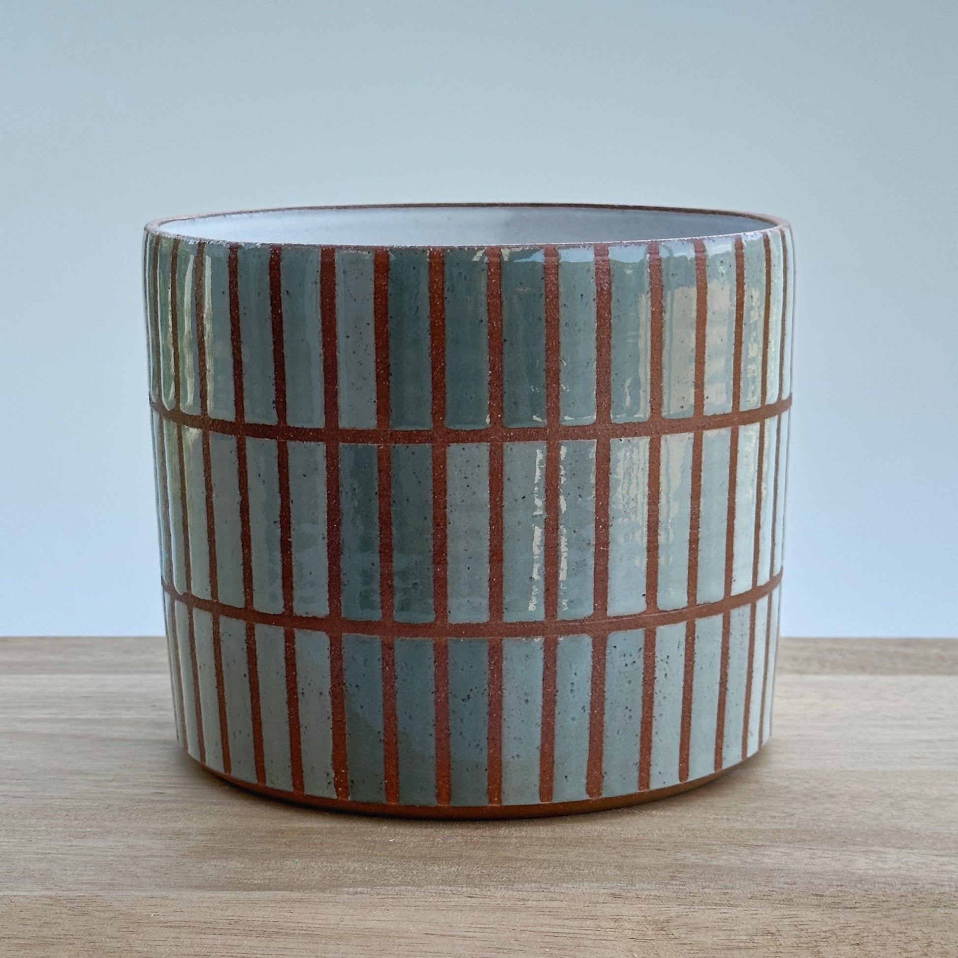 Ceramic pot with vertical striped pattern on a wooden surface and light grey background