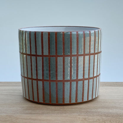 Ceramic pot with vertical striped pattern on a wooden surface and light grey background