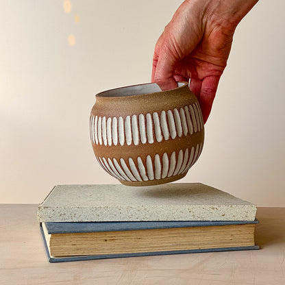 Hand holding a ceramic pot with a textured design on top of two stacked books.