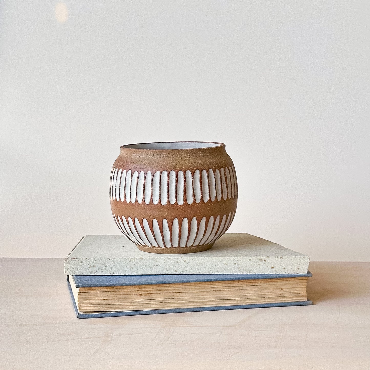 Ceramic pot with white ribbed design on a stack of books against a light background
