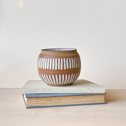 Ceramic pot with white ribbed design on a stack of books against a light background