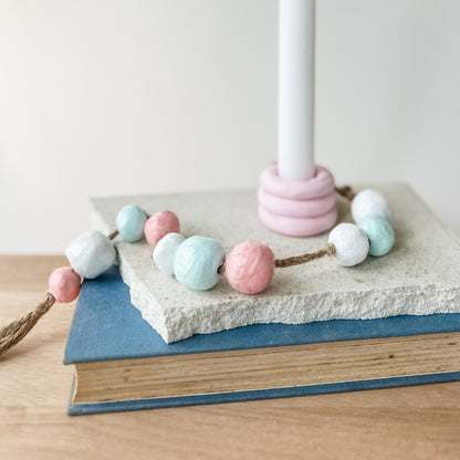 Air-dry clay candle holder with pastel clay beads on a book