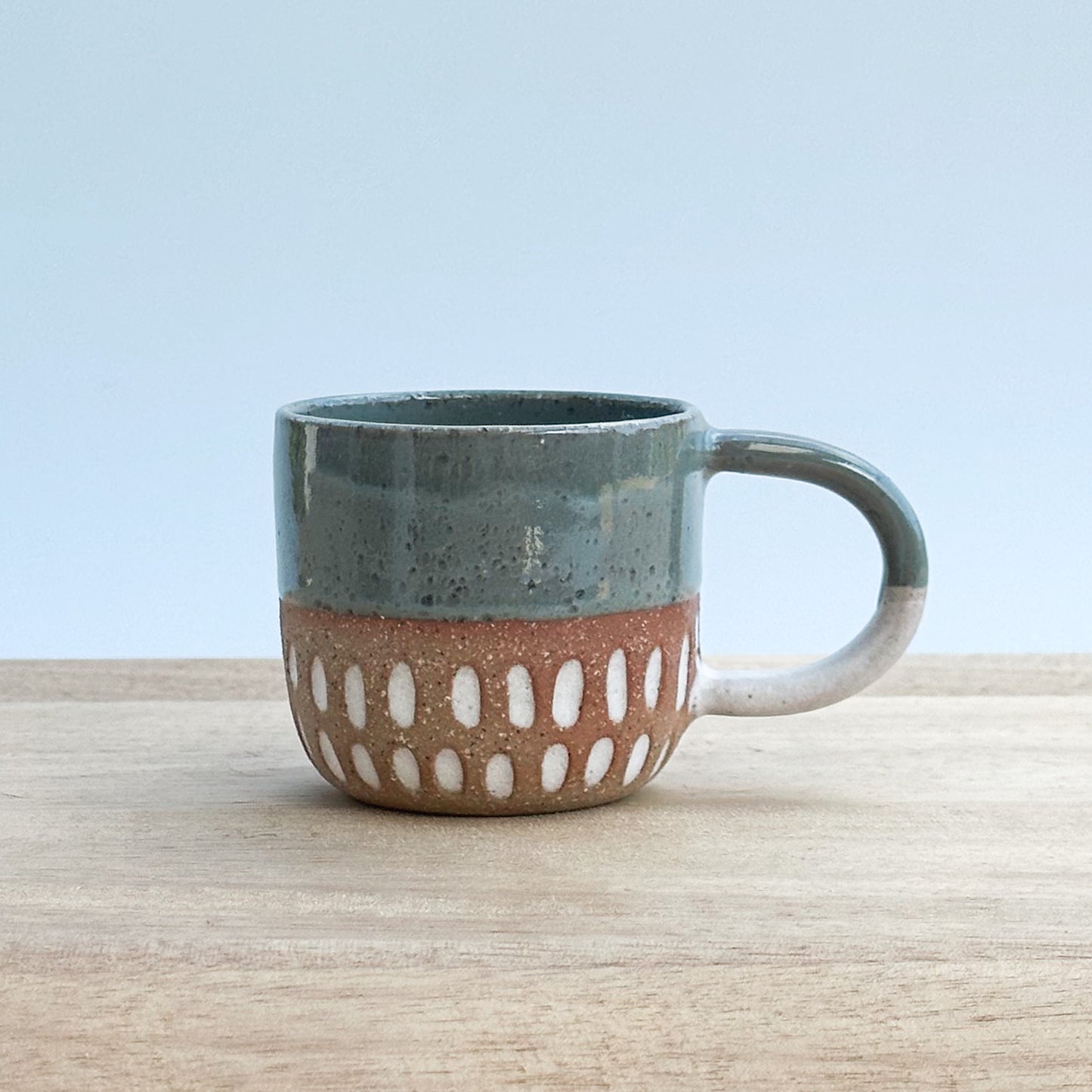 Ceramic espresso mug with a textured design on a wooden surface and a light background