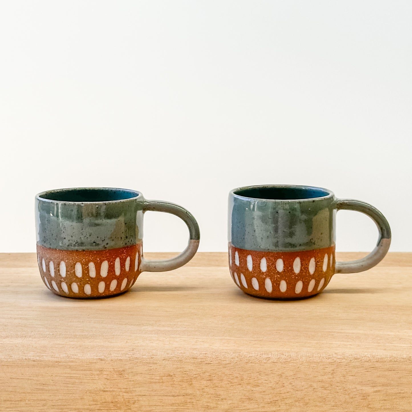 Two espresso ceramic mugs with a carved dot pattern on a wooden surface