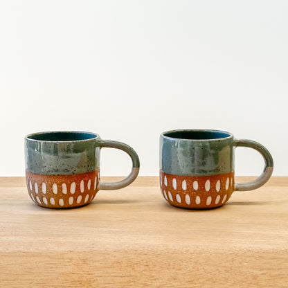 Two espresso ceramic mugs with a carved dot pattern on a wooden surface