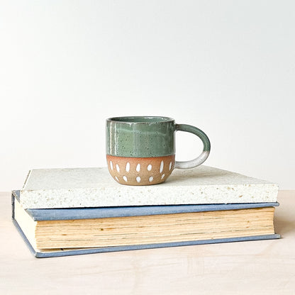 Green espresso ceramic mug with cut-out design on a stack of books against a white background