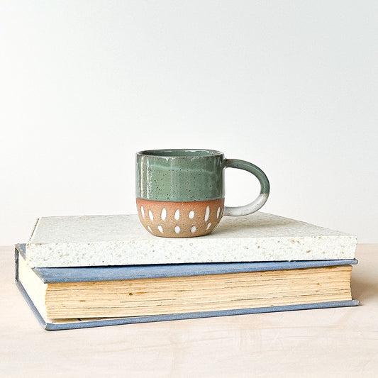 Green espresso ceramic mug with cut-out design on a stack of books against a white background