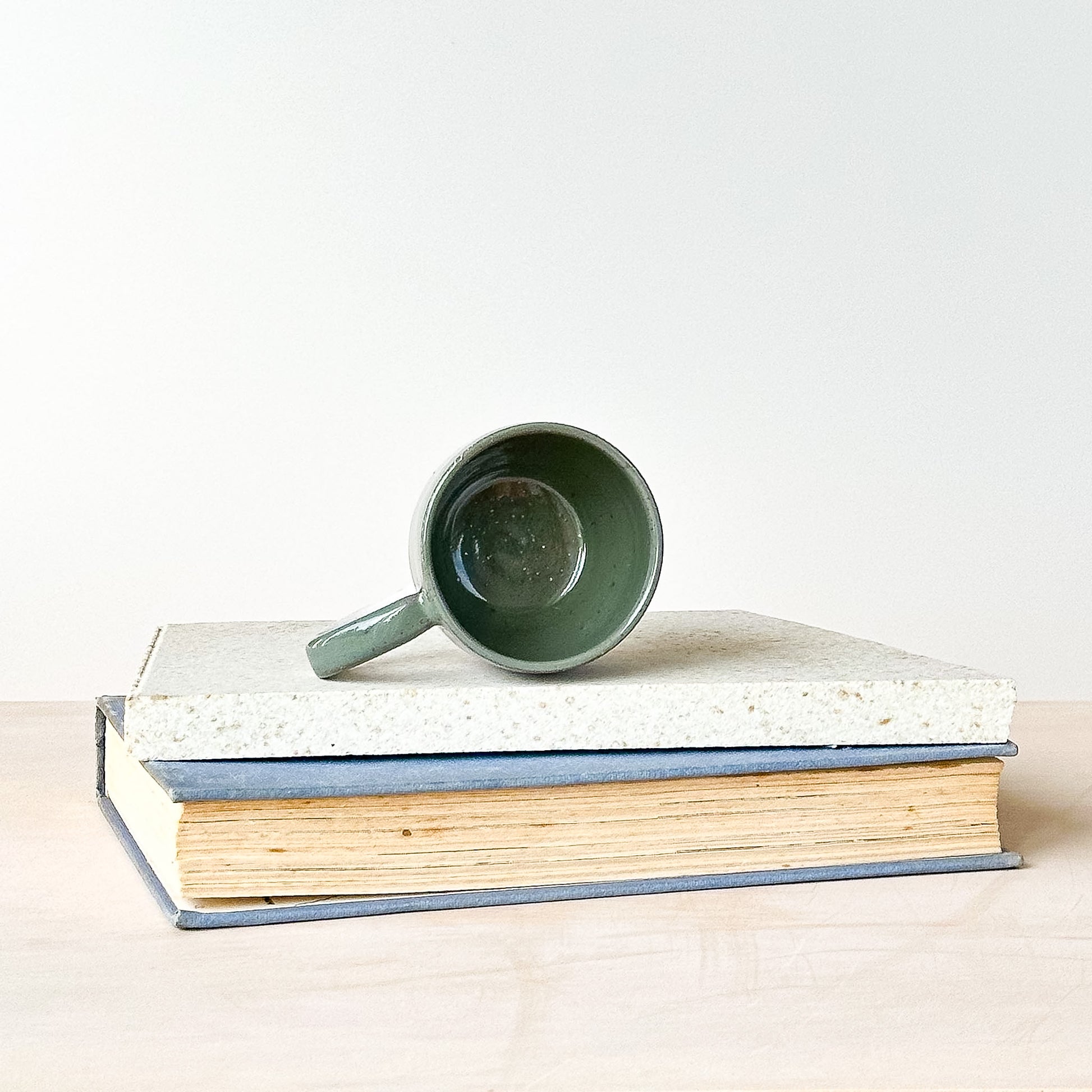 Green espresso mug on top of two stacked books with a plain background