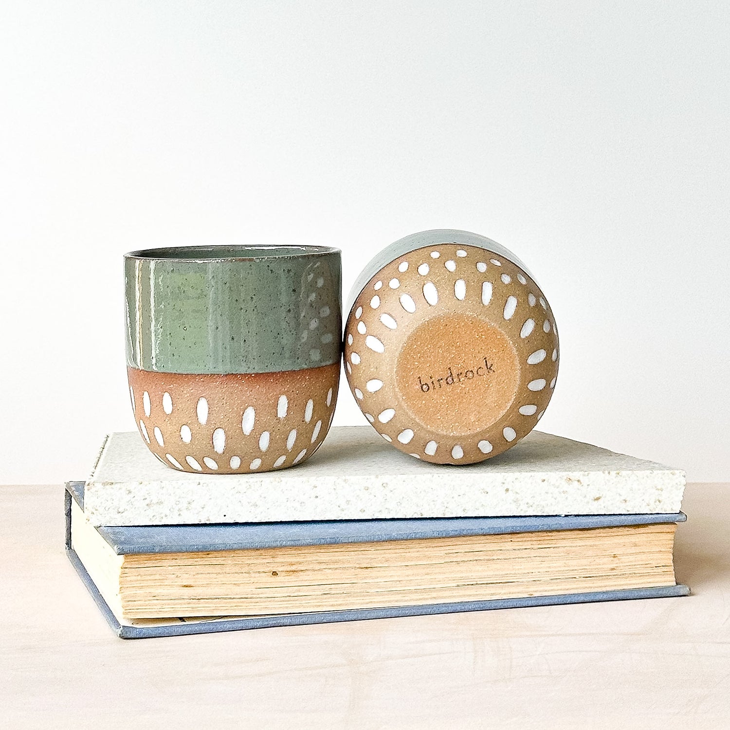 Two ceramic containers with perforated designs on a stack of books, branded 'birdrock'.
