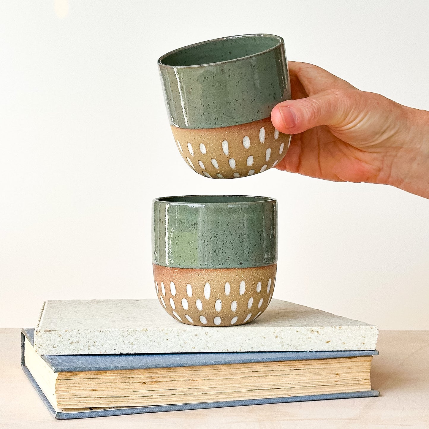 Hand holding a ceramic cup with a textured design on a white background