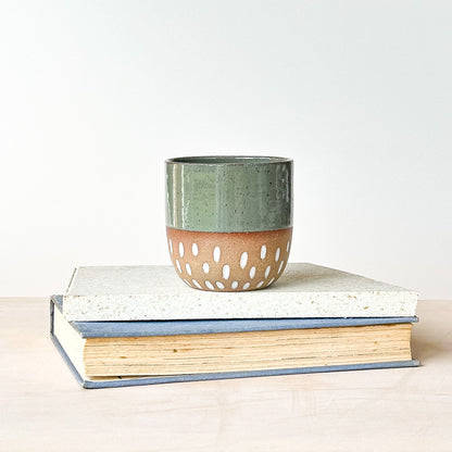 Green ceramic tumbler with a brown base on top of two books against a white background